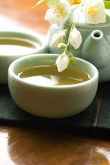 Obraz na płótnie Canvas Zielona herbata z jaśminem w filiżance i czajniczek na drewnianym stole