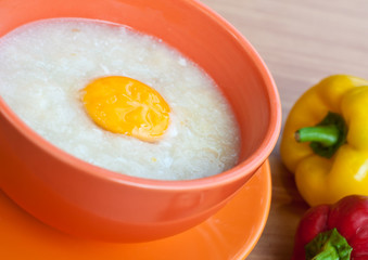 Rice porridge with egg in orange bowl.