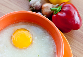 Rice porridge with egg in orange bowl.