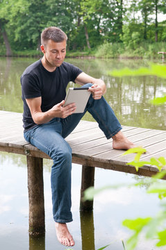 Mann entspannt am See sitzend, mit tablet pc