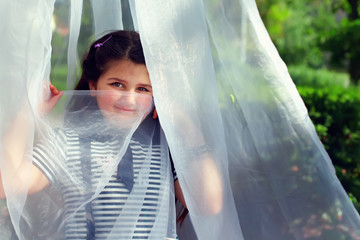 cute little girl hiding face behind transparent tissue in summer