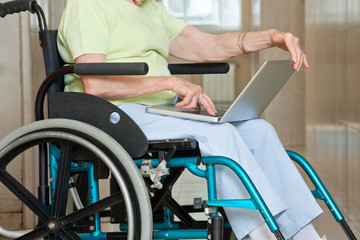 Fototapeta na wymiar Senior Woman Sitting In Wheelchair Using Laptop