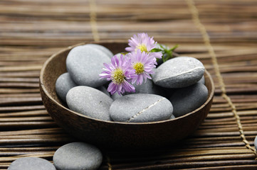 Fototapeta na wymiar Branch flower with zen stones in bowl on woven mat