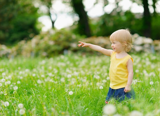 Baby girl on dandelions field pointing on copy space
