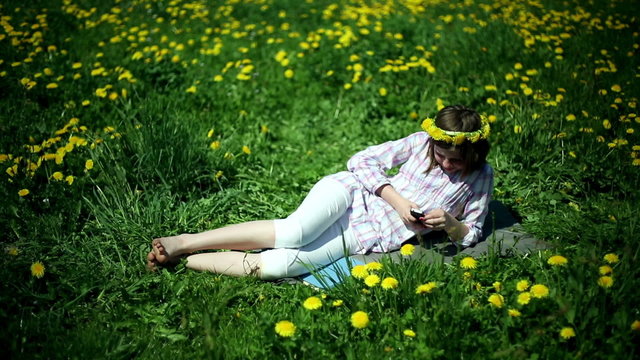 Teenager girl lying on meadow full of sow-thistle with cellphone