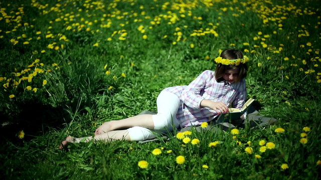 Teenager girl lying on meadow full of sow-thistle reading book