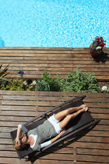 Woman relaxing in deck chair by swimming pool
