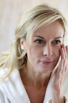 Attractive middle-aged woman applying comestics on her face