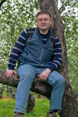 Young man in glasses sitting on a tree and smiling
