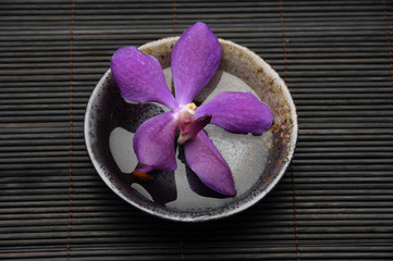 Purple orchids in wooden bowl on bamboo stick straw mat