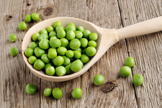 Fresh peas in spoon on wooden background