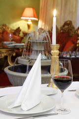 glass with wine, white napkin and candle at table