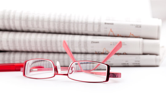 reading glasses lie before a big newspaper pile