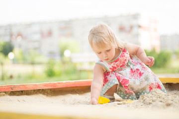 Fototapeta premium Adorable toddler girl in dress play with sand on sandbox