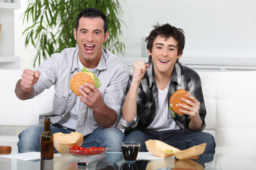 Father and son eating burgers in front of TV