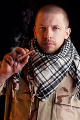 Soldier in combat uniform smoking cigar, over dark background