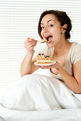 Young Caucasian female sitting in bed with a cake