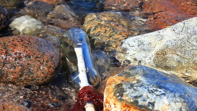 Flaschenpost zwischen Felsen und Wasser am Strand
