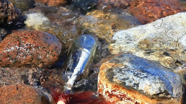 Flaschenpost zwischen Felsen und Wasser am Strand