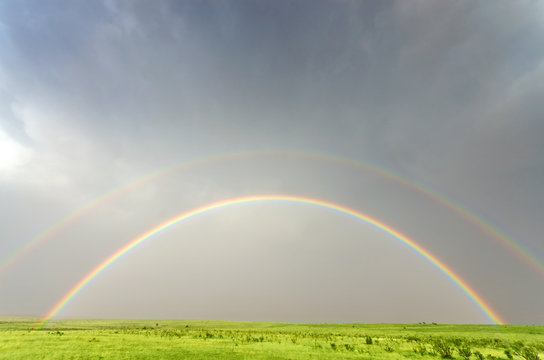 Vivid double rainbow against a green field - Powered by Adobe