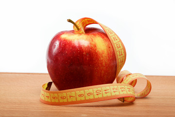 Red apple and measuring tape on a woodtn table.