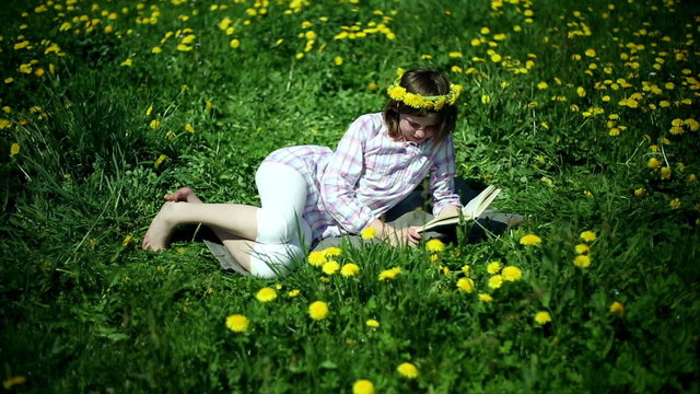 Teenager girl lying on meadow full of sow-thistle and reading