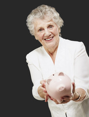 portrait of senior woman showing a piggy bank over black backgro