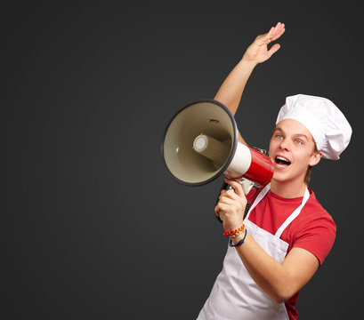 portrait of young cook man shouting with megaphone over black ba