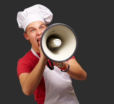 portrait of young cook man screaming with megaphone over black b