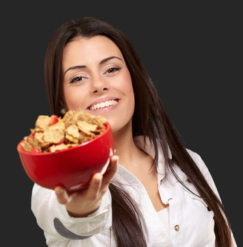 portrait of young woman offering cereals bowl over black backgro