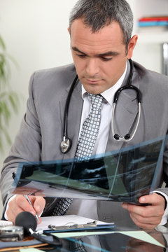 Doctor taking written notes whilst examining x-ray image