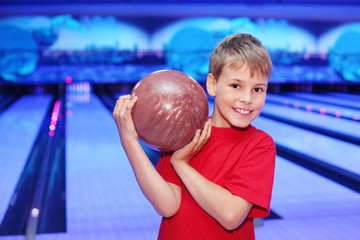 Little smiling boy holds ball in bowling club
