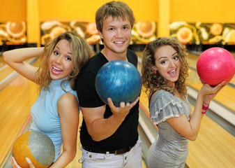 Two happy beautiful girls and man hold balls in bowling club