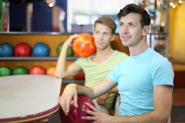 Fototapeta premium Two men sit at table in bowling, hold balls and look up