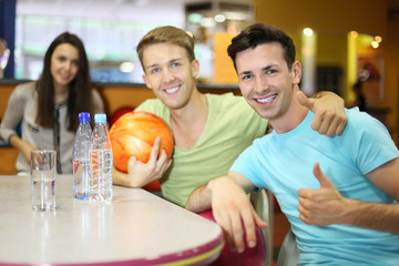 Two men and woman with balls sit at table in bowling