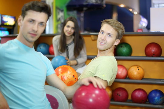 Two men and woman sit near shelves with balls and hold balls