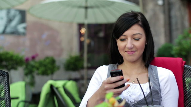 Happy woman drinking cocktail and using smartphone in cafe