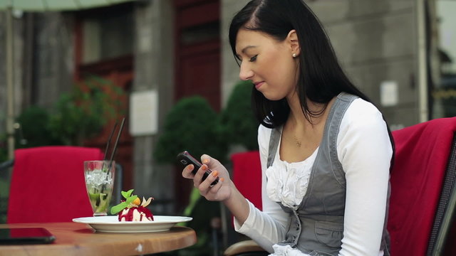 Happy woman eating dessert and using smartphone in cafe