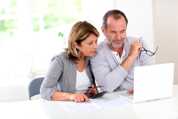 Couple reading construction plan at home with use of laptop