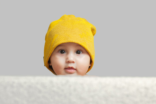 Cute Baby with a Beanie Hat behind a Sofa