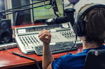 Dj working in front of a microphone on the radio, from the back