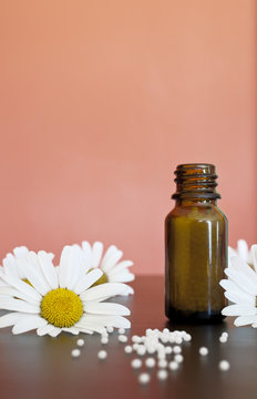 Globuli mit Kamillenbl&uuml;ten vor rotem Hintergrund mit Fl&auml;schchen