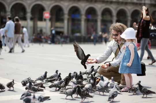 Adorable little girl and her father feeding pigeons