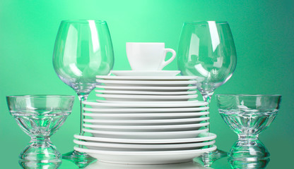Clean plates, cup and glasses on green background