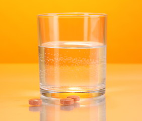 Glass of water and pills on orange background