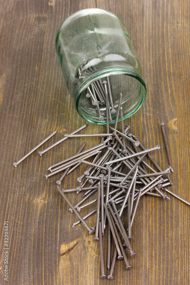 Wall mural Metal nails and glass jar on wooden background