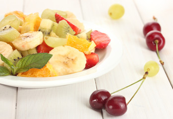Fresh fruits salad on plate and berries on white wooden table