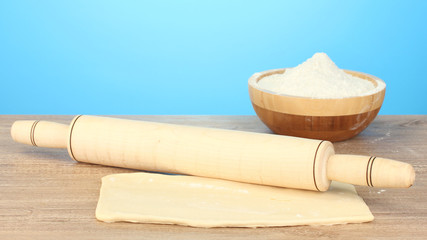 the dough with a rolling pin on wooden table on blue background