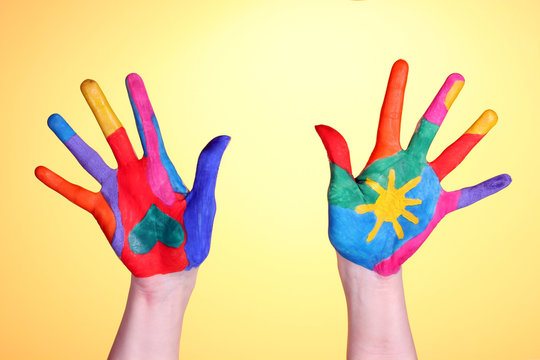 Brightly colored hands on yellow background close-up