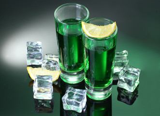 Two glasses of absinthe, lemon and ice on green background